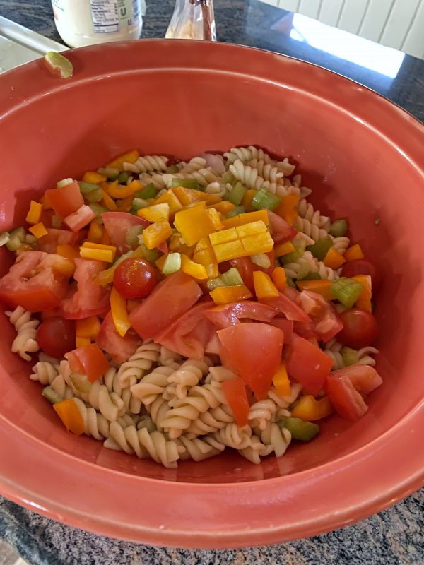 Adding choppedcheese nd vegetables to large orange bowl for tuna pasta salad